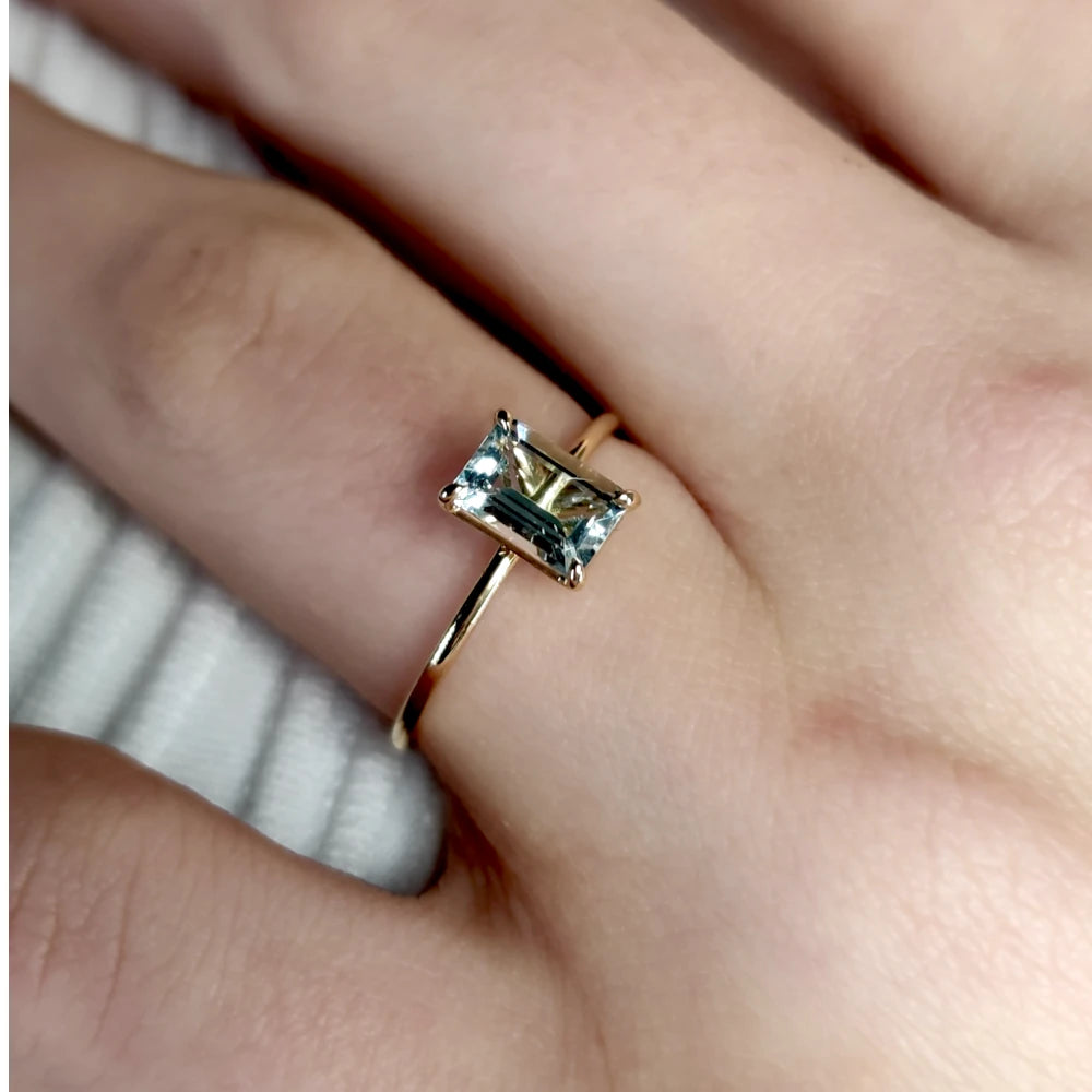 Timeless 18K yellow gold solitaire aquamarine ring displayed on a model’s hand