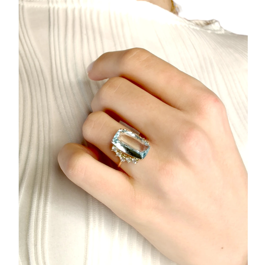 Elegant engagement ring featuring a rectangular cushion aquamarine and diamonds in 14K yellow gold worn on a model’s hand