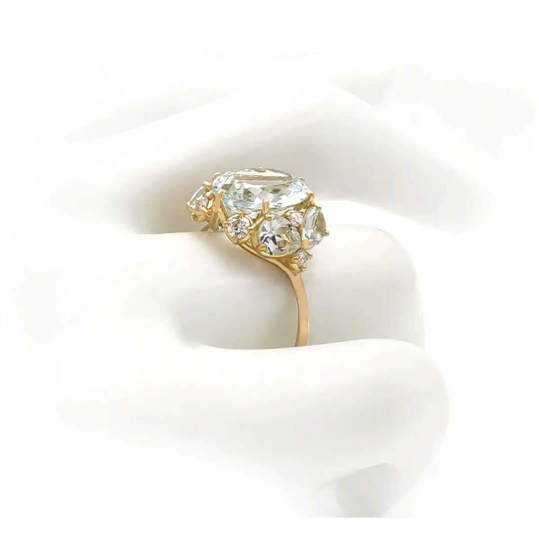 Side view of a handcrafted 18K yellow gold engagement ring on a mannequin hand, featuring natural aquamarines and brilliant diamonds, ideal for buyers seeking a unique ring.