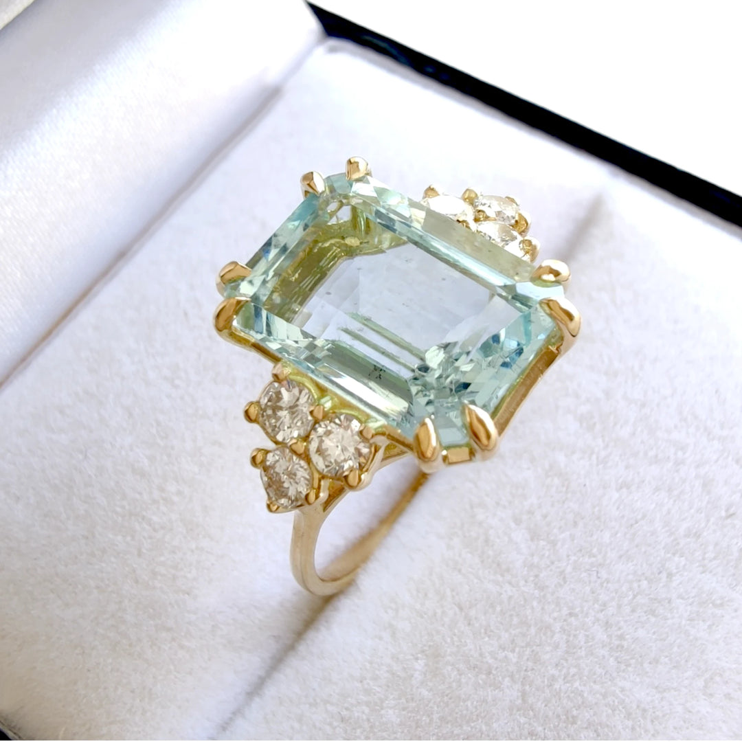 18K yellow gold engagement ring with a large emerald-cut aquamarine and diamonds, elegantly placed inside a jewelry box, perfect for those looking to buy a special gift.