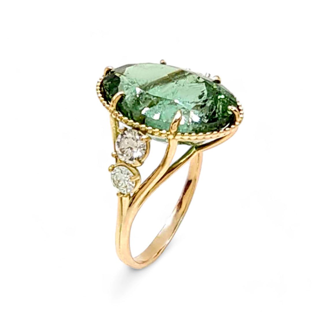 Closeup vertical view of a 14K yellow gold cocktail ring featuring a central oval green tourmaline with miligrain detailing and two diamonds on each side, perfect for a Christmas gift or special occasion