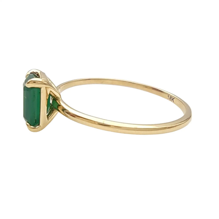 Left side view of a solitaire emerald engagement ring in 18K yellow gold, showcasing the ring’s sleek band and stunning gemstone setting