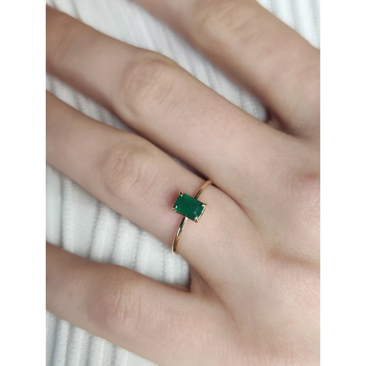 Top view of a model’s hand wearing an 18K yellow gold solitaire emerald engagement ring, highlighting the gemstone's vibrant color and timeless style