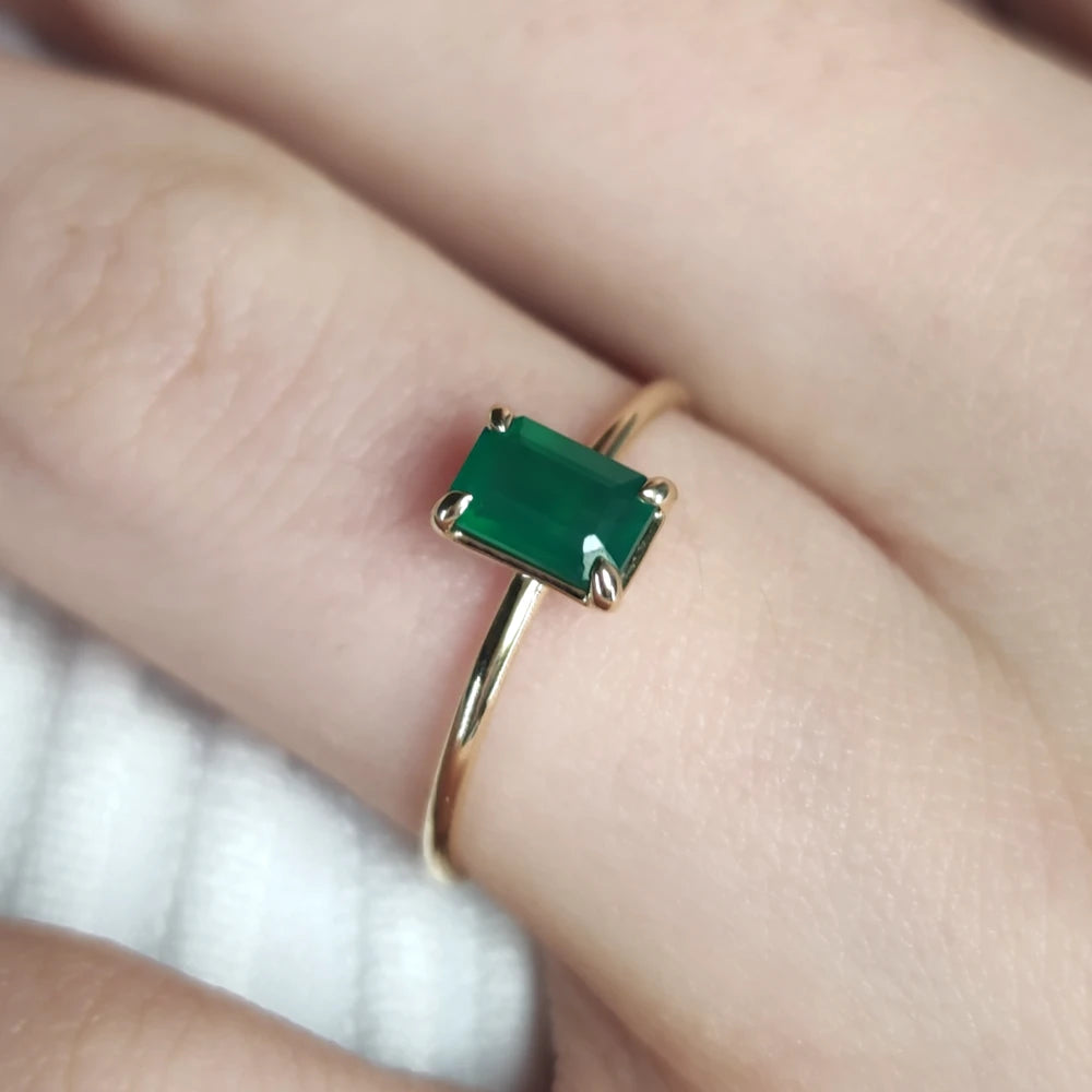 Close-up detail of a model’s finger adorned with an 18K yellow gold emerald solitaire engagement ring, showcasing its luxurious simplicity and elegance