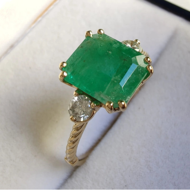 18K yellow gold engagement ring featuring a central emerald and diamonds, elegantly presented in a jewelry box, a perfect buy for a romantic Christmas proposal