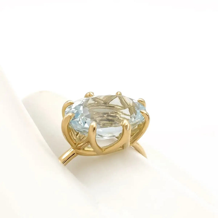 Fourth pose of a mannequin hand displaying a solitaire 18K yellow gold engagement ring with an oval aquamarine, showcasing the ring's design from various angles.