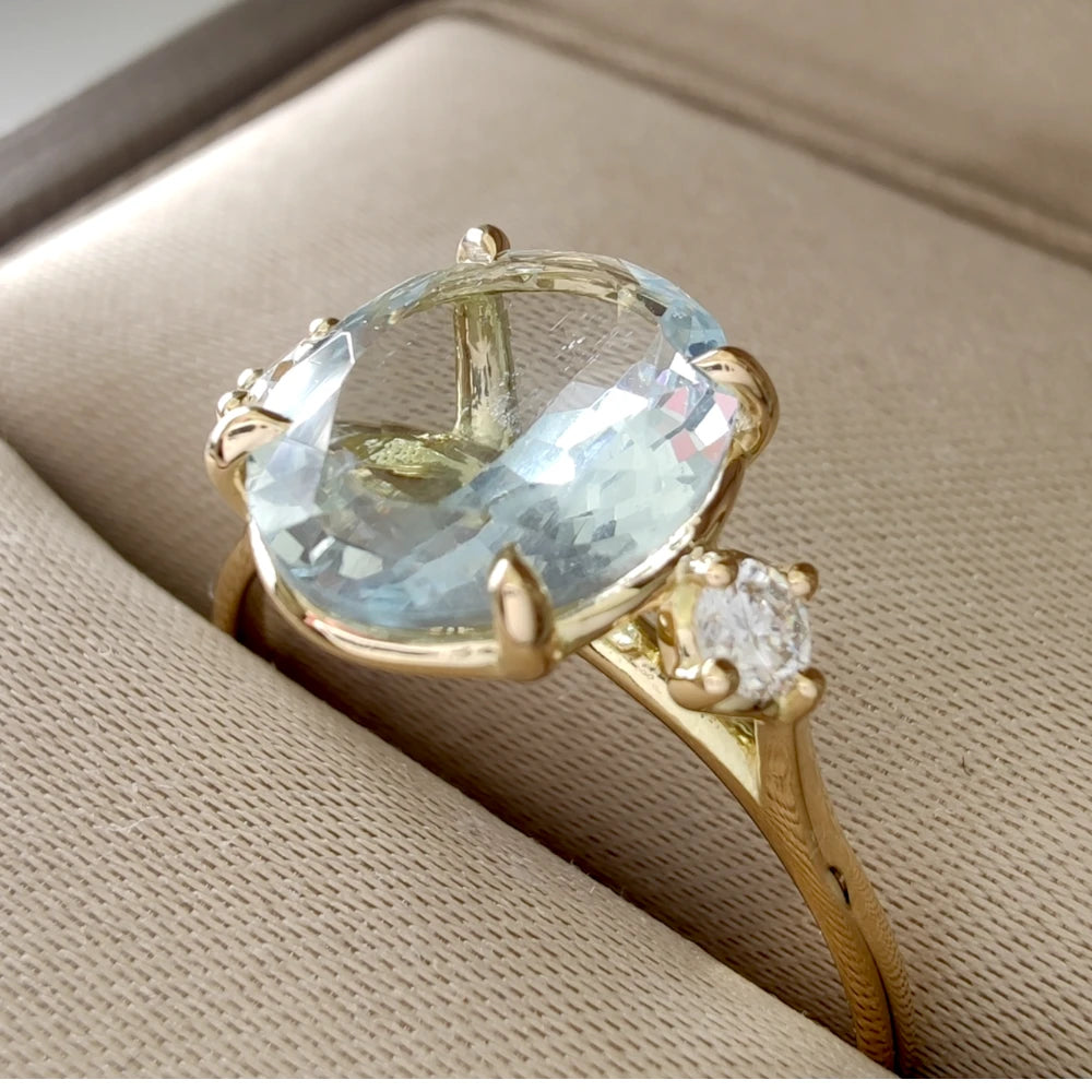 Side view of an 18K yellow gold engagement ring in a jewelry box, highlighting the oval aquamarine and side diamonds, perfect for special occasion gifting