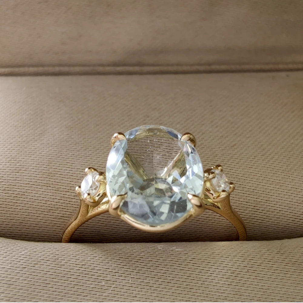 Top view of an 18K yellow gold engagement ring featuring an oval aquamarine and diamonds, elegantly presented in a jewelry box, ideal for buyers looking for a luxurious gift