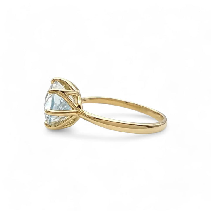 Left side horizontal view of a solitaire 18K yellow gold engagement ring with a central oval aquamarine, emphasizing its sleek and modern design for engagements