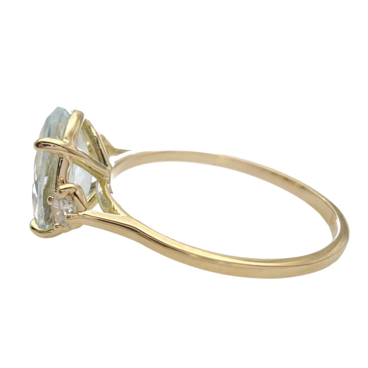 Left horizontal side view of an 18K yellow gold three-stone engagement ring, showcasing a light blue oval aquamarine and brilliant diamonds, available for purchase