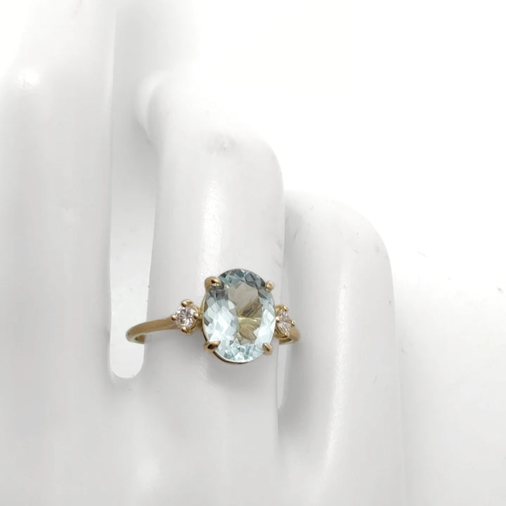 Various poses of a mannequin hand displaying an 18K yellow gold engagement ring with an oval aquamarine and diamonds, showcasing different angles and features of the ring