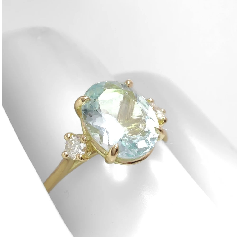 Side view of an 18K yellow gold three-stone engagement ring on a mannequin hand, showcasing a central oval aquamarine and diamonds, ideal to buy for a special occasion