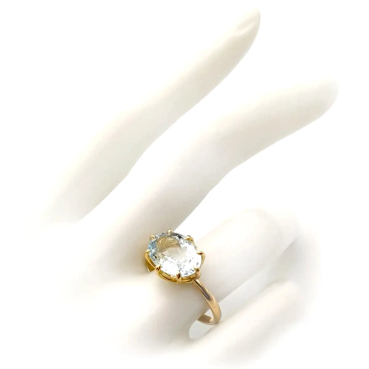 18K yellow gold solitaire engagement ring with an oval aquamarine displayed on a mannequin hand, showcasing its elegant basket setting, perfect for proposals