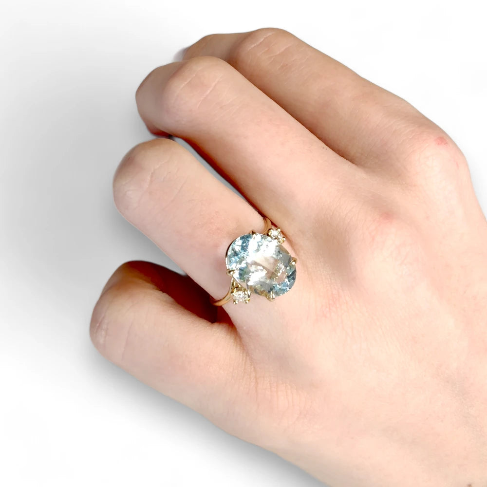 18K yellow gold engagement ring worn by a female model, featuring a central oval aquamarine and diamonds on the sides, perfect to buy as a thoughtful gift