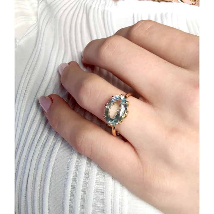 Model hand displaying a solitaire 18K yellow gold engagement ring with a central oval aquamarine, emphasizing its suitability for engagement and special occasions