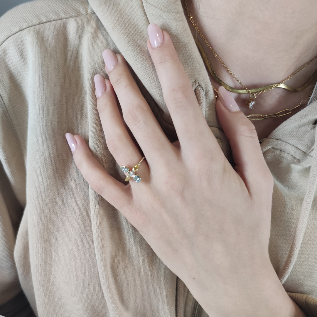 Second pose of a model's hand showing a 14K yellow gold engagement ring with miligrain details and a central brilliant diamond surrounded by fancy colored diamonds, showcasing its luxurious and intricate craftsmanship