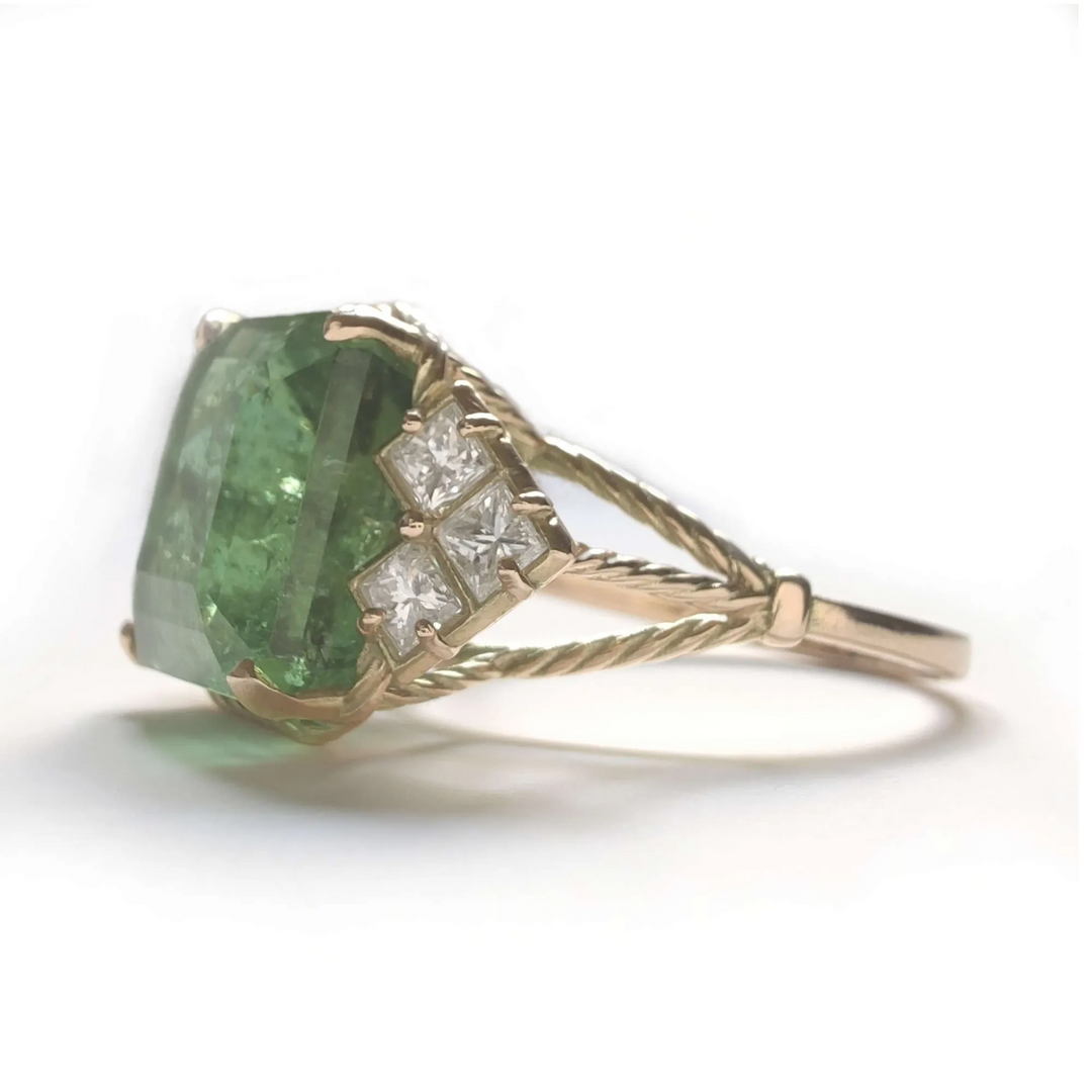 Left side view of a 14K yellow gold engagement ring with a green tourmaline and princess-cut diamonds, emphasizing the vintage design and curled band details