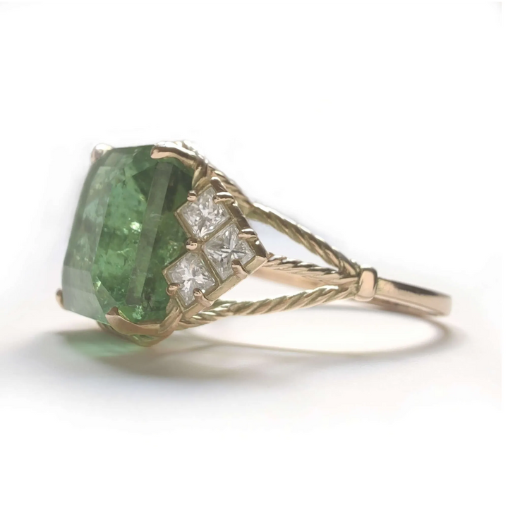 Left side view of a 14K yellow gold engagement ring with a green tourmaline and princess-cut diamonds, emphasizing the vintage design and curled band details