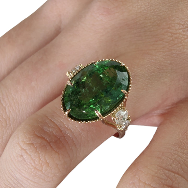 Third pose of a model's hand featuring a 14K yellow gold cocktail ring with a central oval green tourmaline and diamonds, showcasing the ring's artistic and contemporary quality