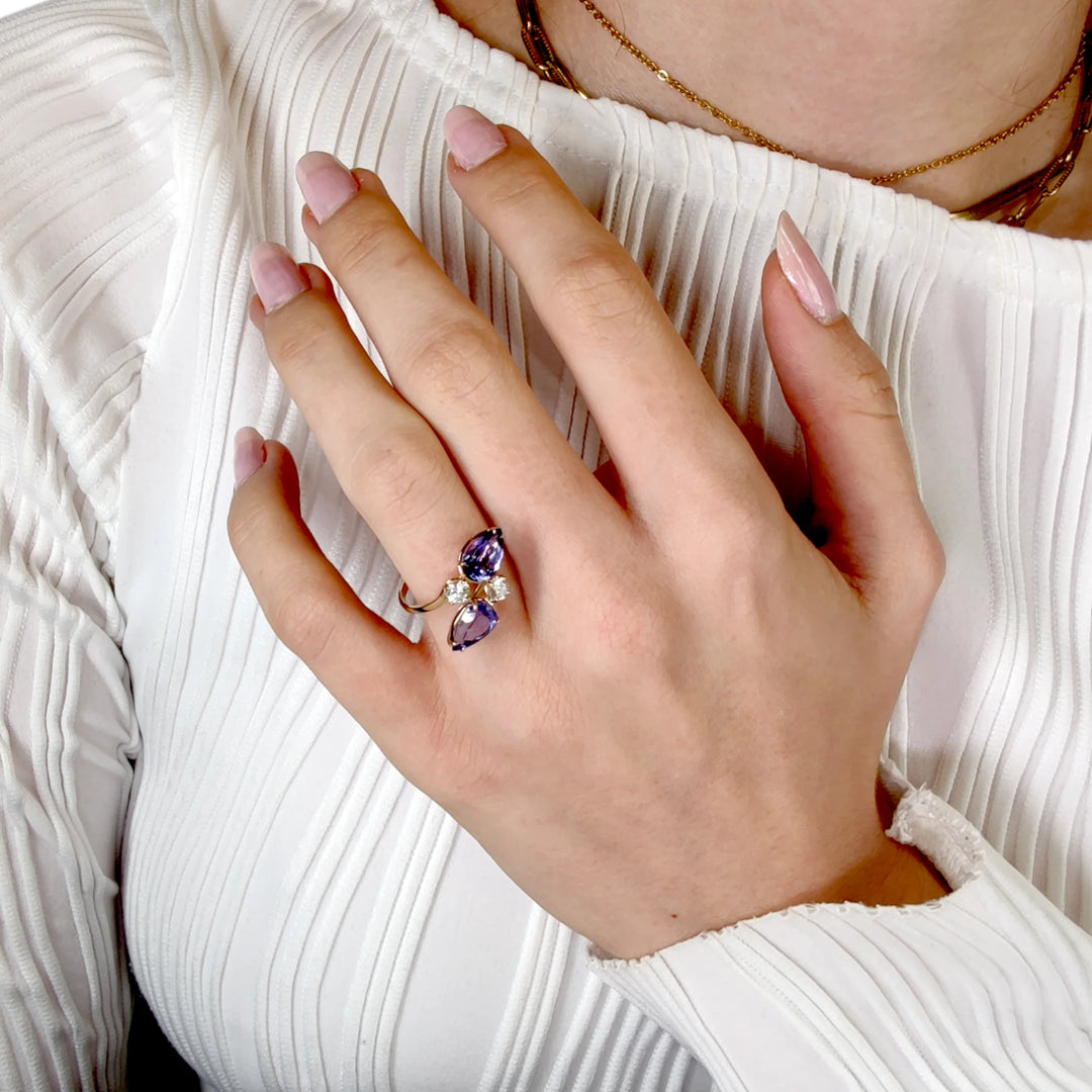 First pose of a female model's hand displaying a 14K yellow gold bypass engagement ring with pear-cut tanzanite and brilliant diamonds, emphasizing the ring's elegant design