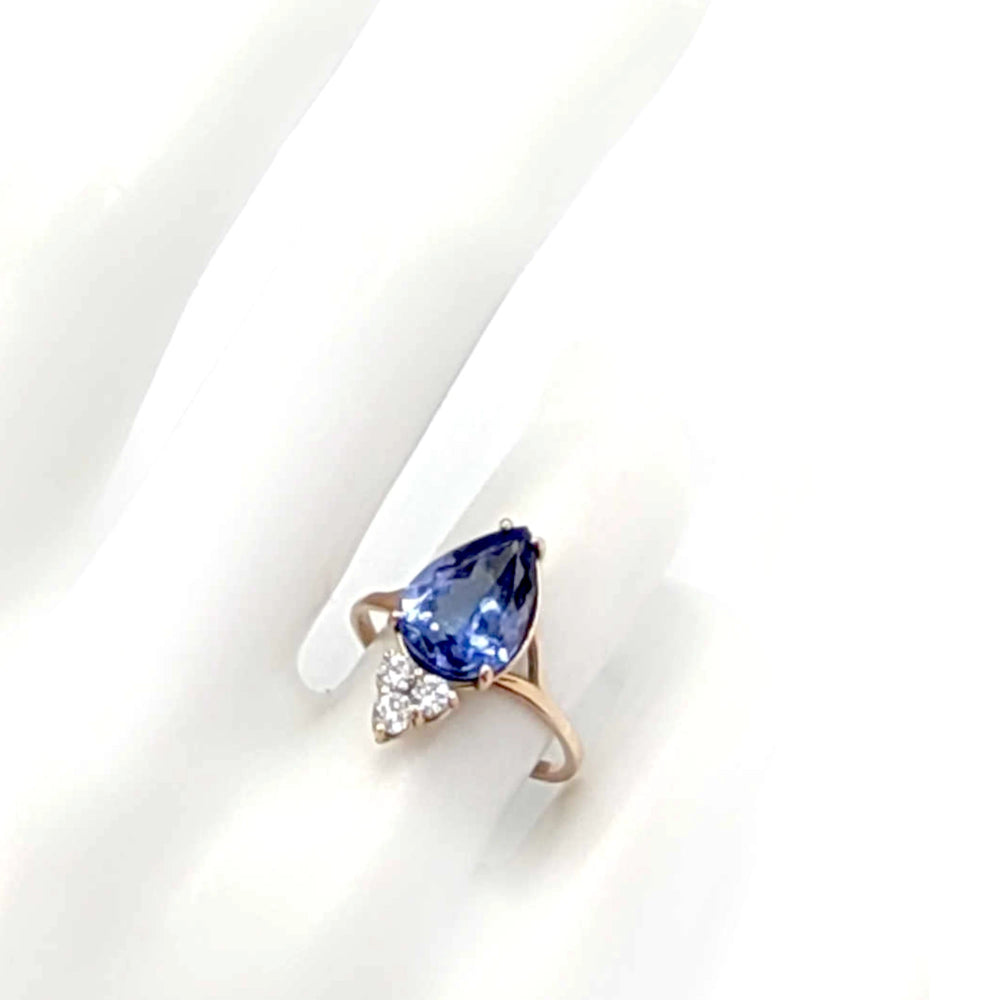 Top view of a 14K yellow gold engagement ring on a mannequin hand, showcasing a central pear-cut tanzanite and three brilliant diamonds, ideal for those looking for a unique, handmade engagement ring