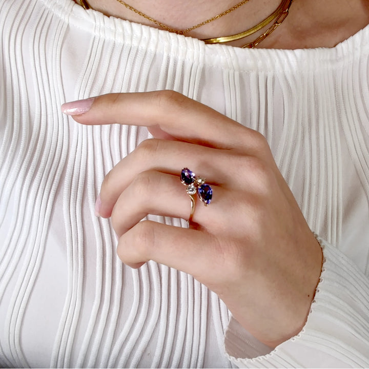 Third pose of a model's hand displaying a 14K yellow gold engagement ring with pear-cut tanzanite and diamonds, highlighting the luxurious and contemporary design