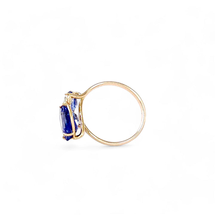 Left side view of a 14K yellow gold engagement ring with pear-cut tanzanite and brilliant diamonds, showcasing the bypass design and elegant gem setting