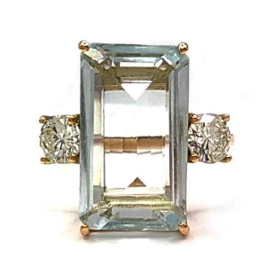 A 14K yellow gold three-stone engagement ring for women, featuring a central aquamarine flanked by a diamond on each side, showcasing a timeless and elegant design perfect for a proposal or as a meaningful gift