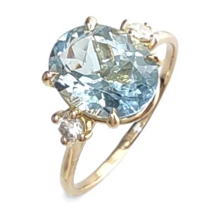 Front view of an 18K yellow gold three-stone engagement ring featuring a central oval aquamarine with a diamond on each side, perfectly blending classic elegance with contemporary design for a memorable proposal or special gift