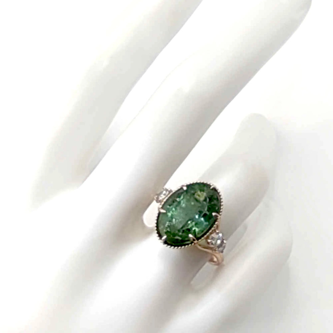 14K yellow gold cocktail ring on a mannequin hand showcasing a central oval green tourmaline and diamonds, highlighting the ring's contemporary design and certified gemstones