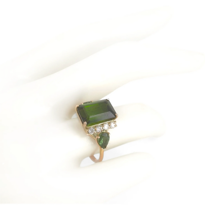 Front view of a 14K yellow gold engagement ring on a mannequin hand, showcasing a dark green emerald-cut tourmaline with brilliant diamonds and pear-shaped tourmalines, ideal for those looking for a contemporary ring