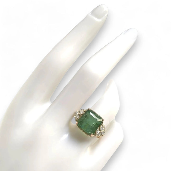 Top view of a 14K yellow gold engagement ring on a mannequin hand, highlighting a green tourmaline center and princess-cut diamonds in a vintage-style setting with curled arms, ideal for buyers looking for a unique and romantic gift