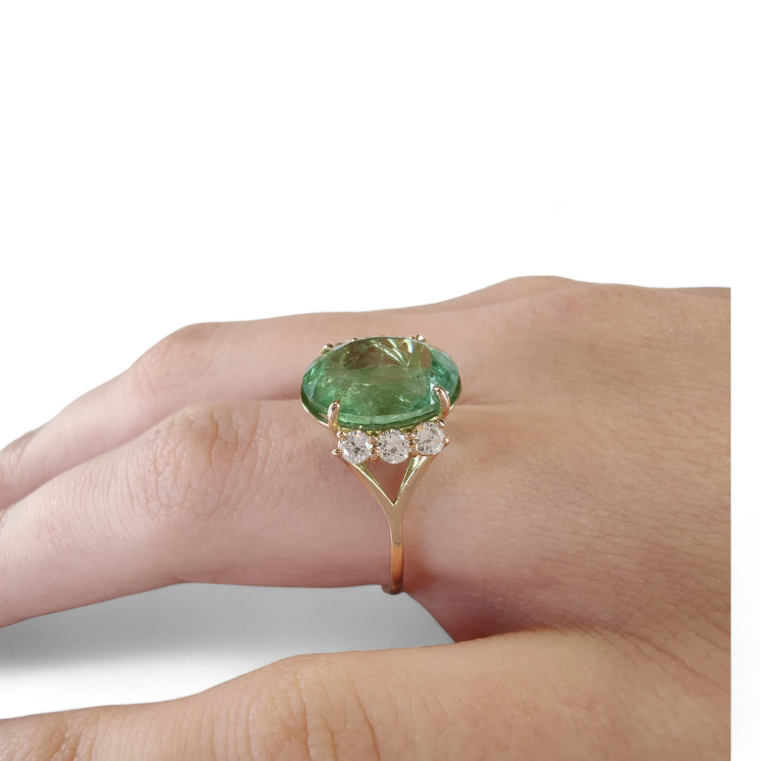 First pose of a model's hand displaying a 14K yellow gold engagement ring with a central oval green tourmaline and diamonds, emphasizing the ring's elegance and unique design.