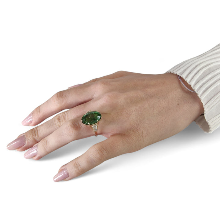 Full hand view of a model wearing a 14K yellow gold cocktail ring with an oval green tourmaline and diamonds, showcasing the ring's contemporary design and appeal