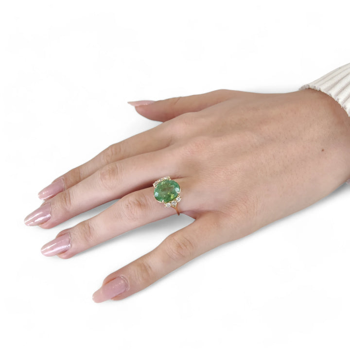 Full hand view of a model wearing a 14K yellow gold engagement ring with an oval green tourmaline and diamonds, showcasing the ring's modern style and appeal