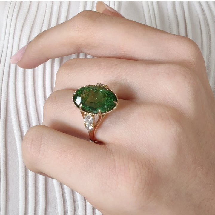 Second pose of a model wearing a 14K yellow gold ring with an oval green tourmaline and diamonds, highlighting the sophisticated design and miligrain detailing.