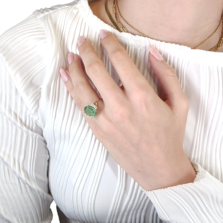 Third pose of a model's hand featuring a 14K yellow gold engagement ring with a central oval green tourmaline and diamonds, showcasing the ring's artistic and handmade quality.