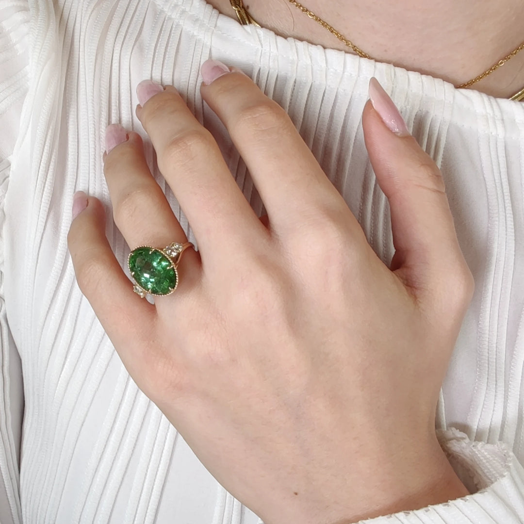 Fourth pose of a model's hand displaying a 14K yellow gold cocktail ring with an oval green tourmaline and diamonds, highlighting the ring's unique style and certified gemstones