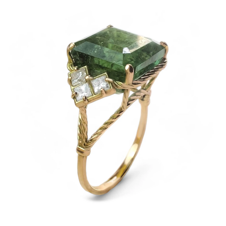 Slightly twisted vertical view of a 14K yellow gold vintage-style engagement ring featuring a green tourmaline with three princess-cut diamonds on each side, showcasing intricate curled arms, perfect for Christmas or as a gift for a special woman in your life