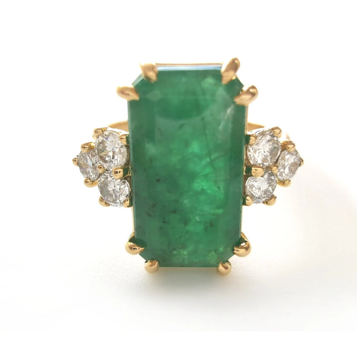 Front view of a fine 18K yellow gold engagement ring with a central emerald and three round diamonds on each side

