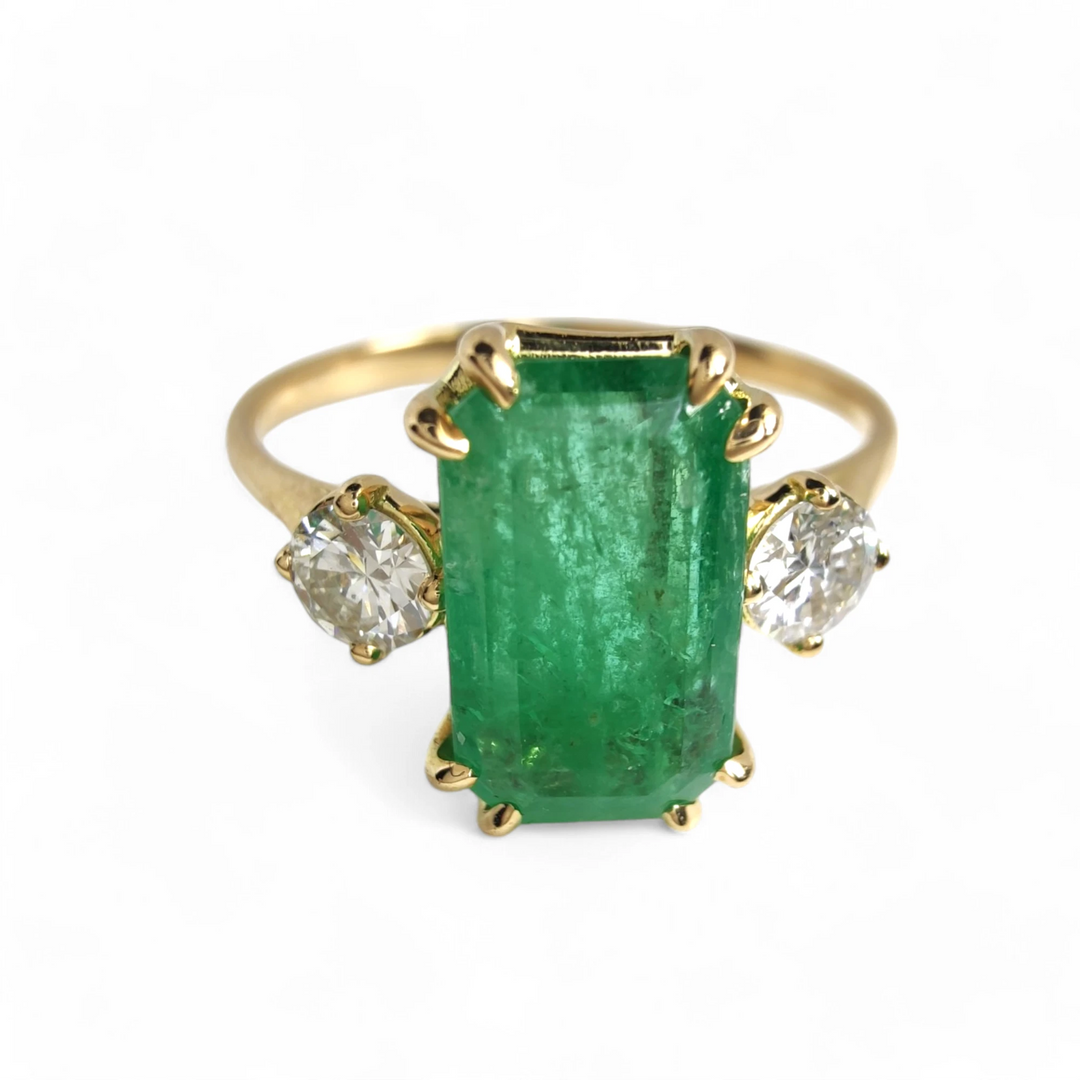 Front view of a timeless three-stone engagement ring in 18K yellow gold with a central emerald and diamonds, perfect for proposals or Christmas gifts