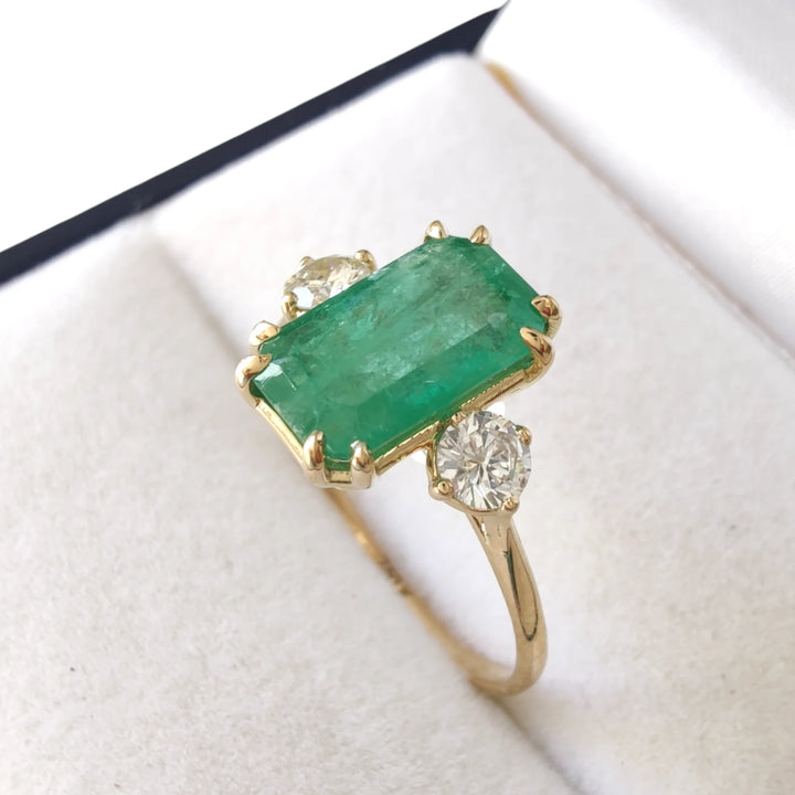 Beautiful emerald engagement ring in 18K yellow gold with diamond accents, displayed inside a jewelry gift box, perfect for proposals or holiday gifts