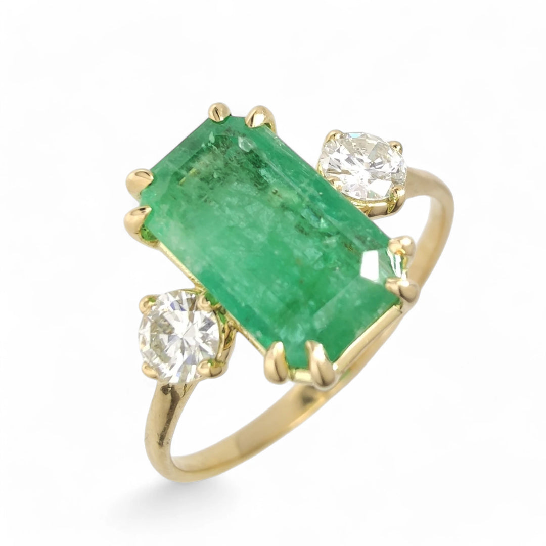 Vertical perspective view from above of an 18K yellow gold engagement ring featuring a central emerald and a diamond on each side, perfect as a Black Friday or Christmas gift