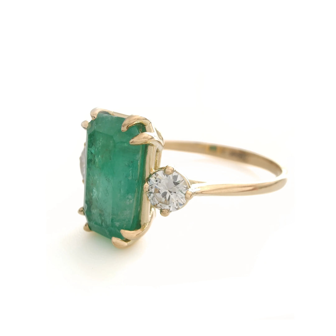 Left side view of a classic engagement ring in 18K yellow gold featuring a central emerald and diamonds, perfect for Black Friday gifting