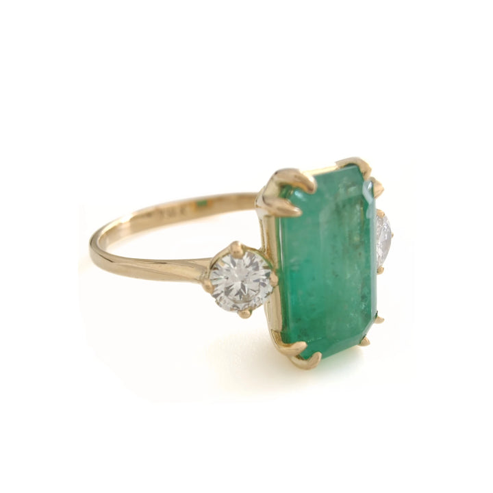 Right side view of an elegant 18K yellow gold three-stone engagement ring with a central emerald and diamonds