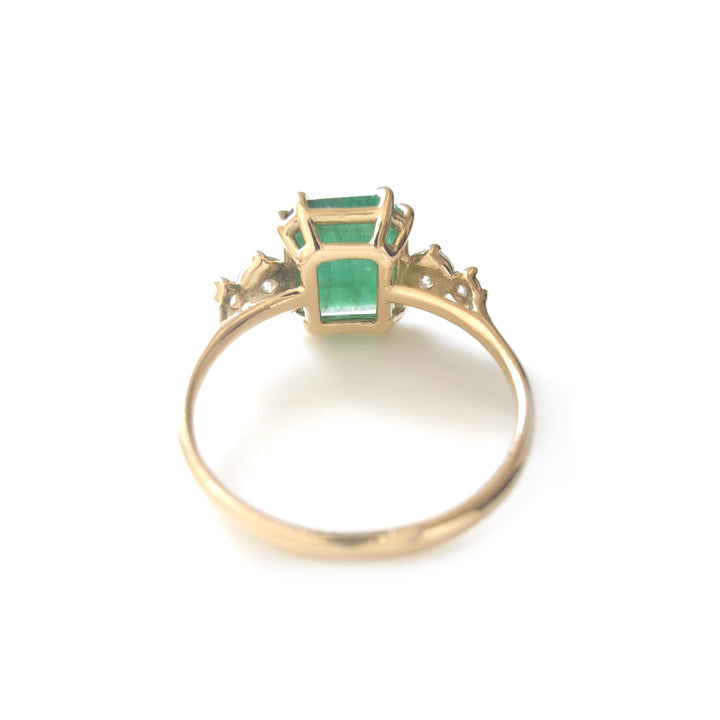 Back view of a 18K yellow gold engagement ring showcasing the central emerald and diamond detailing