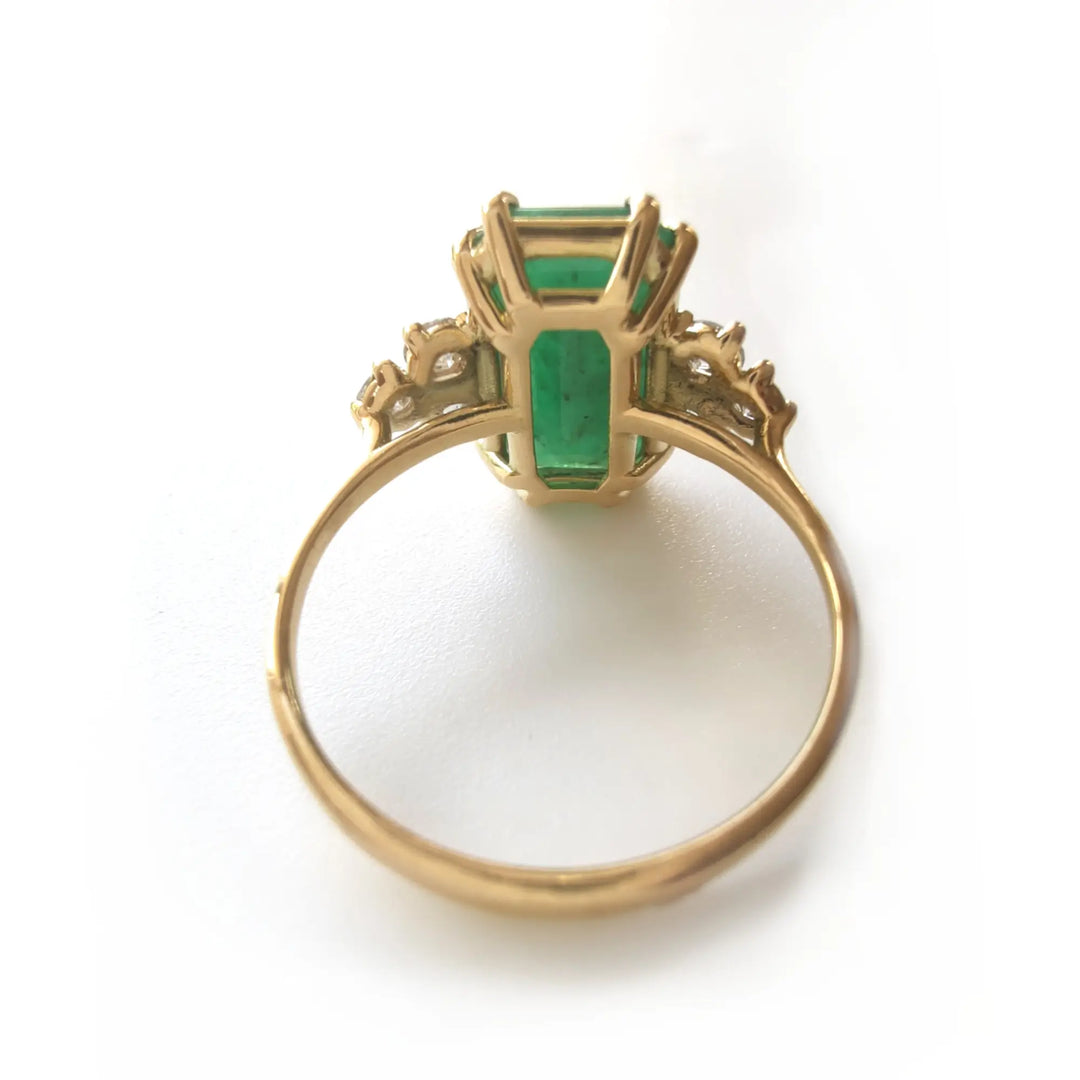 Back view of an elegant engagement ring in 18K yellow gold with an emerald centerpiece and diamond accents, ideal for fine jewelry lovers