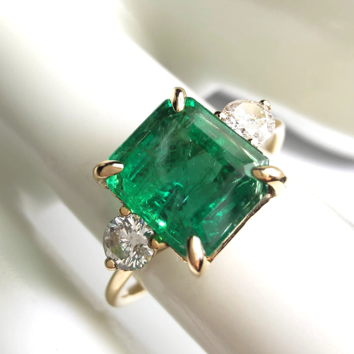 Close-up of a women’s three-stone ring in 18K yellow gold with an emerald cut emerald and diamond side stones