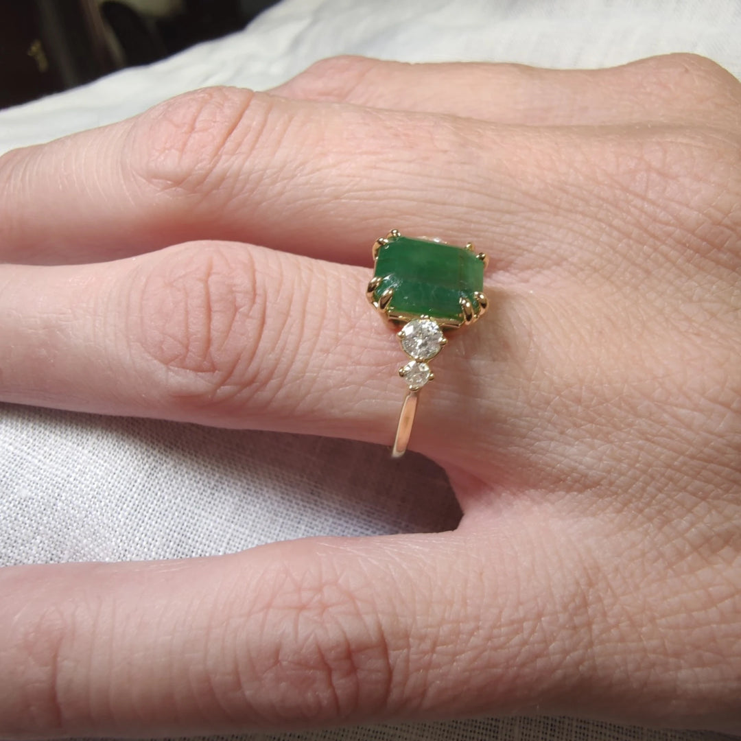 Close-up detail of a women’s engagement ring in 18K yellow gold with an emerald cut emerald and round diamonds displayed on a model’s hand