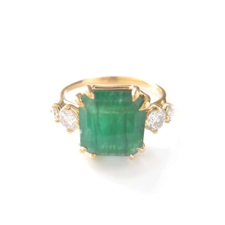 Front view of a stunning engagement ring in 18K yellow gold with a central emerald cut emerald and round diamonds on each side

